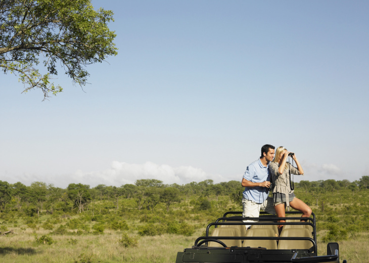 couple dans une Jeep en plein safari dans la savane avec des jumelles